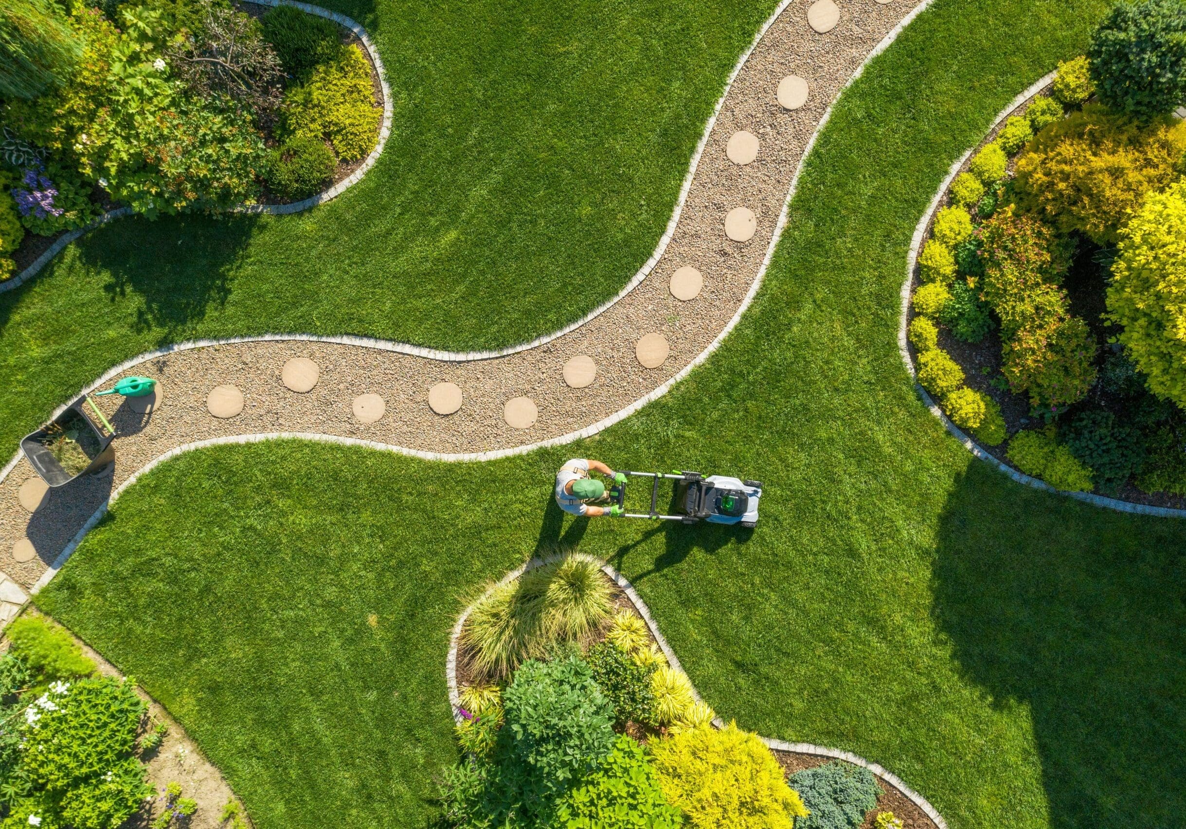 aerial view of a person moving a neatly landscaped lawn with stone walkways and garden beds